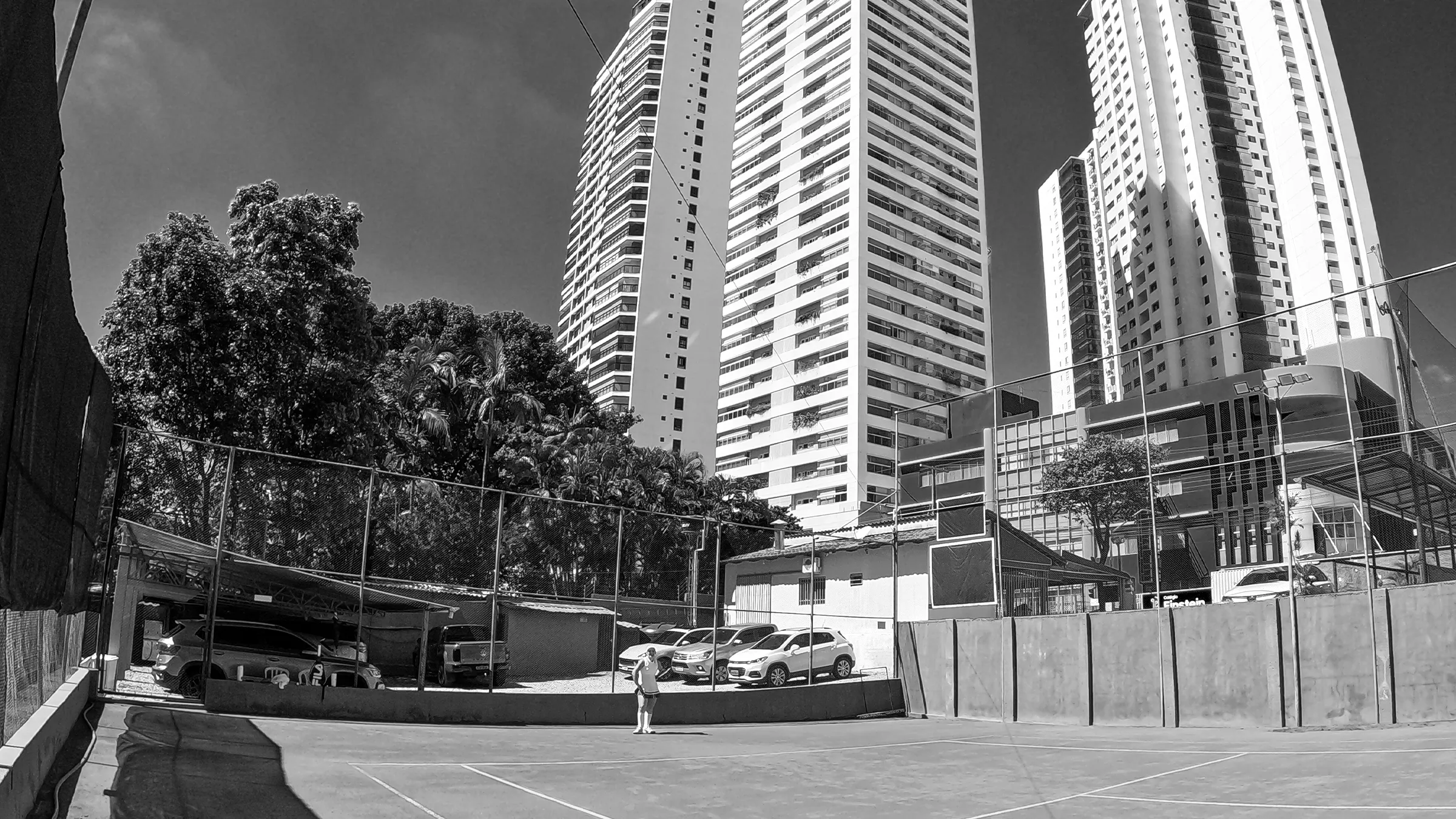 Quadra da Bueno Tennis Club, em Goiânia, fotografada de baixo com prédios ao fundo, em preto e branco.