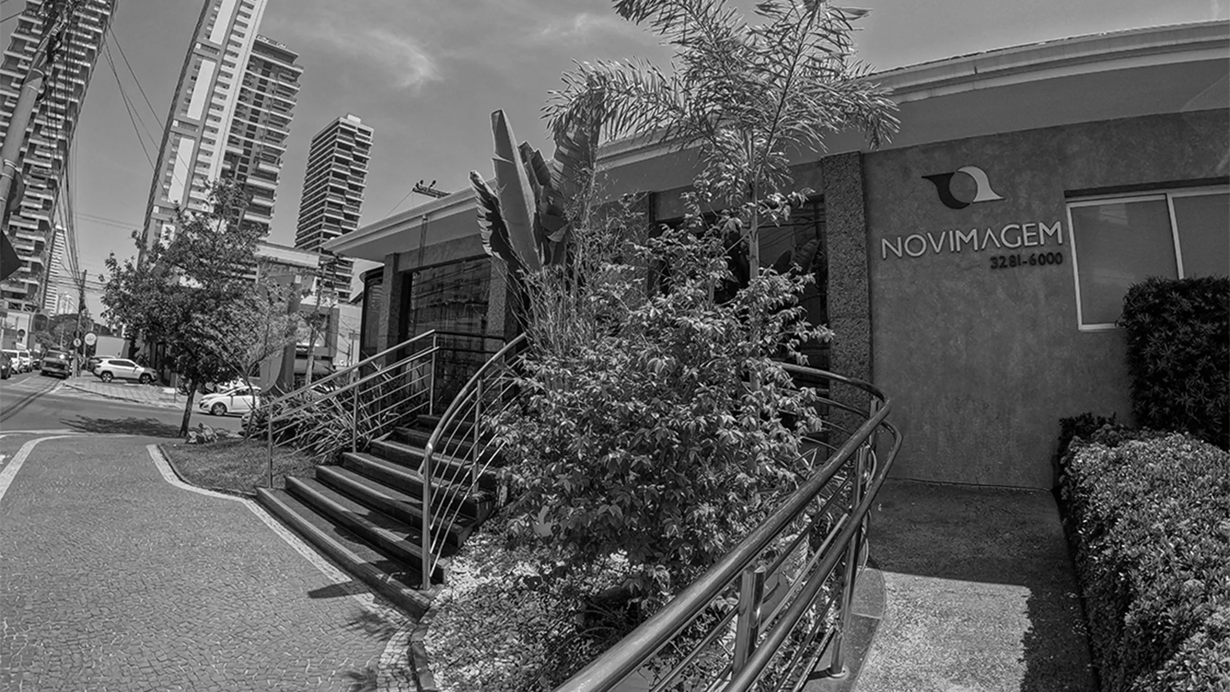 Fachada da Novimagem em Goiânia, com a marca aplicada na parede e jardim em primeiro plano, em preto e branco.